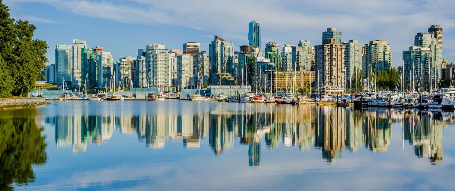 Vancouver skyline with high-rise buildings and marina reflections on calm water, in a sunny day, capturing urban development and waterfront scenery.